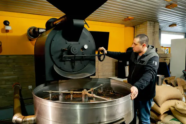 Küçük bir kızartma fabrikasında bir işçi kızartma makinesinin yanında duruyor ve kızarma derecesini izliyor.