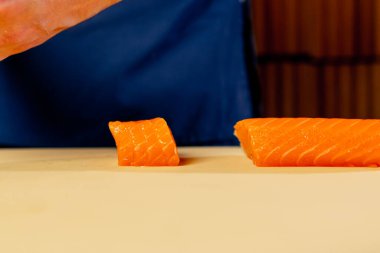 Japon lokantasında mavi üniformalı bir şef suşi için balık kesiyor.