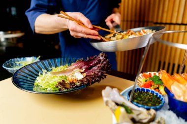 Japon restoranına yakın çekim yapan mavi elbiseli bir şef pahalı bir tabak deniz ürünü hazırlar.