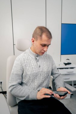 Klinikte yakın plan. Açık renk kazaklı genç bir adam, kulak tıkayıcı bir doktorla görüşüyor.