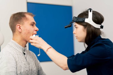 Klinikte genç bir doktor kulağının burun kısmı hastanın boğazını muayene ediyor.