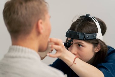 Klinikte genç bir doktor kulağının burun kısmı hastanın boğazını muayene ediyor.