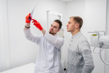 Özel bir klinikte, beyaz bir röntgen odasında doktor hastaya sırtının resmini gösterir.