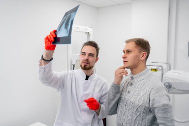 Özel bir klinikte, beyaz bir röntgen odasında doktor hastaya sırtının resmini gösterir.