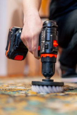 Daireyi kapatın. Bir usta temizlikçi tornavida ve fırçayla halıyı deterjanla temizler.