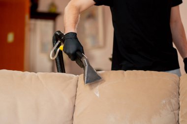 Bir dairede profesyonel temizliği kapatmak. Temizlikçi yıkamadan önce tekstil kanepesini ıslatır.