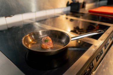 Profesyonel bir mutfakta bir parça tavuk fileto küçük bir tavada kızarır.