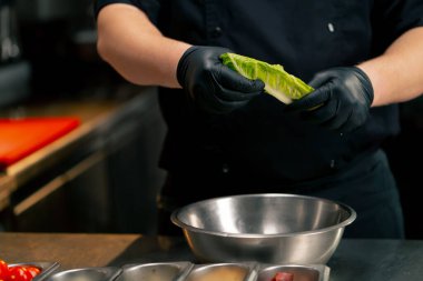 Profesyonel bir mutfakta yakın plan çekimde şef marul yapraklarını demir bir klozete parçalar.