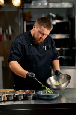 Profesyonel bir mutfakta şef, marul parçalarını bir tabağa cımbızla koyar.