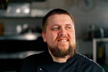 Mutfakta siyah ceketli bir şefin profesyonel bir portresi var. Gülümse.