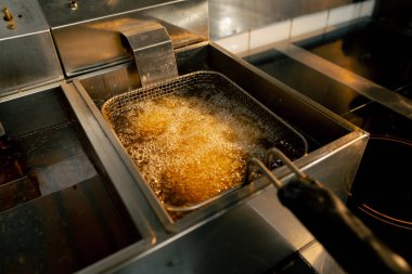 Profesyonel bir mutfakta yakın plan çekimde tavuk kanatlarını fritözde kızartıyorum.