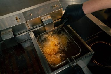 Profesyonel bir mutfakta yakın plan çekimde tavuk kanatlarını fritözde kızartıyorum.