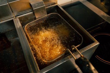 Profesyonel bir mutfakta yakın plan çekimde tavuk kanatlarını fritözde kızartıyorum.