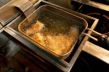 Profesyonel bir mutfakta tavuk kanatlarının kızartıldığı yakın çekim.