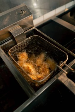 Profesyonel bir mutfakta yakın plan çekimde tavuk kanatlarını fritözde kızartıyorum.