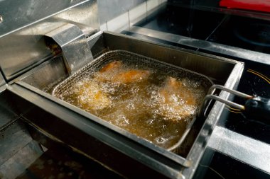 Profesyonel bir mutfakta yakın plan çekimde tavuk kanatlarını fritözde kızartıyorum.