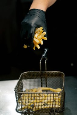 Profesyonel bir mutfak şefine yakın plan siyah eldivenli patates kızartmasını fritöze koyar.