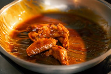 Profesyonel bir mutfakta sosla kızartılan tavuk kanatlarının yakın çekimi.