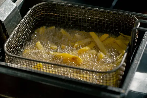 close-up in a professional kitchen frying French fries in oil in a deep fryer