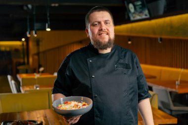 Lokantada siyah ceketli bir şef hazır salata tebessümleriyle kameraya bakar.