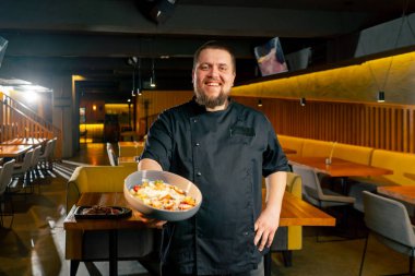 Siyah ceketli bir restoran şefi hazır salatayla gülümsüyor.