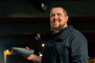 Siyah ceketli bir restoran şefinin yanında hazır salatayla gülümsüyor.