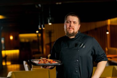 Siyah ceketli bir restoran şefinin yanında hazır tavuk kanatları var.