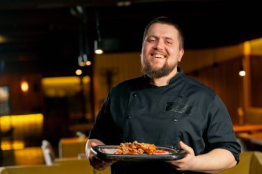 Siyah ceketli bir restoran şefi hazır tavuk kanatlarıyla gülümsüyor.