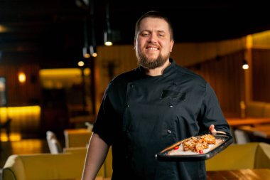 Siyah ceketli bir restoran şefi hazır tavuk kanatlarıyla gülümsüyor.