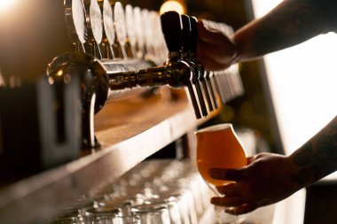 Bar tezgahındaki birahanede yakın plan barmenlerin elleri bardağa hafif bira döker.