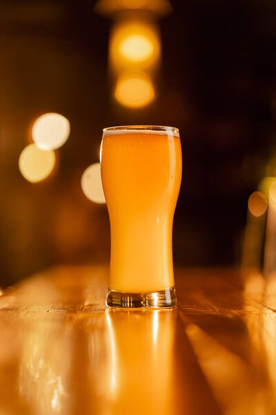 close up in the bar there is a glass of beer on a wooden bar counter in the rays of the sun