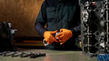 Masadaki bir benzin istasyonunda genç bir motor tamircisi yeni bir piston parçası monte ediyor.