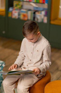 Çocuk mahallesindeki bir kitapçıda hafif giysili yakışıklı bir çocuk kitap okuyor.