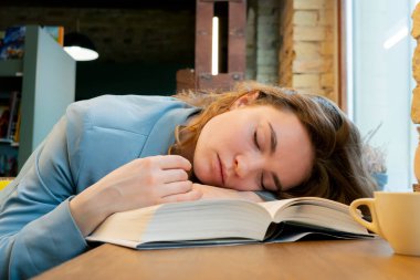 Pencerenin yanındaki bir kitapçıda güzel bir uykucu öğrenci oturuyor ve sınavlara hazırlanıyor.
