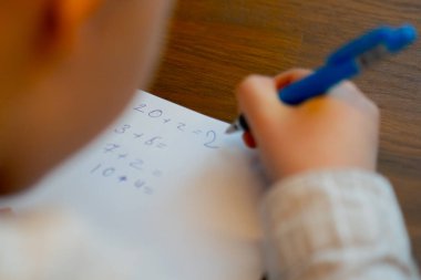 Kitapçıda yakın plan. Masada oturan yakışıklı bir çocuk matematik denklemlerini çözüyor.