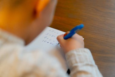 Kitapçıda yakın plan. Masada oturan yakışıklı bir çocuk matematik denklemlerini çözüyor.