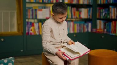 Çocuk mahallesindeki bir kitapçıda hafif giysili yakışıklı bir çocuk kitap okuyor.