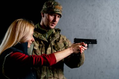 Profesyonel bir atış poligonunda bir asker bir kıza tabancayla doğru duruşu gösterir.