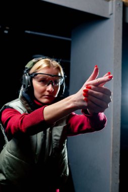 Profesyonel bir atış poligonunda kulaklık ve gözlüklü bir kız tabanca duruşunu eğitiyor.