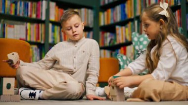 Çocukların olduğu bölgedeki bir kitapçıda uzun saçlı güzel bir kız ve oğlan tahta oyuncaklarla oynuyorlar.