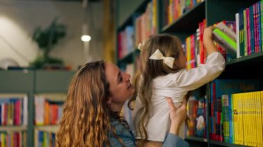 Çocukların olduğu bölgedeki bir kitapçıda bir anne kızının doğru kitaba ulaşmasına yardım eder.