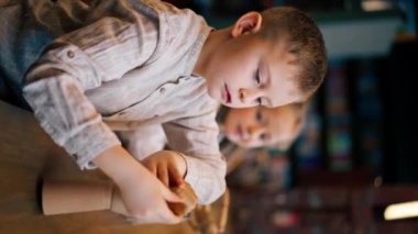 Bir kitapçıdaki dikey video. Masadaki güzel bir kız ve oğlan tahta oyuncaklarla oynuyor.