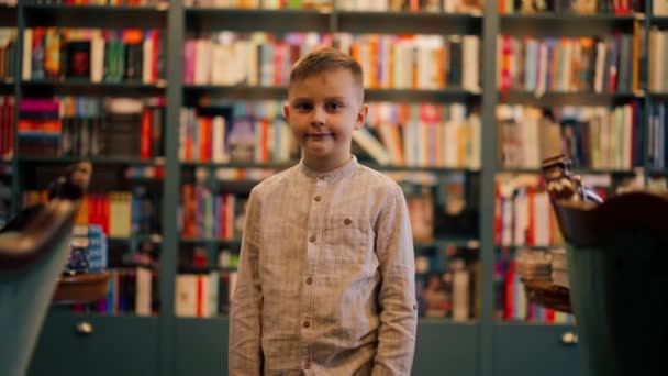 Lähikuva Kirjakaupassa Komea Poika Seisoo Hymyillen Kirjahyllyjen Keskellä Onnellinen Asiakas — kuvapankkivideo
