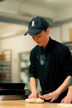 Profesyonel bir mutfakta, siyah tunik giymiş kadın bir fırıncı fırın tepsisindeki ekmek şeklini alır.