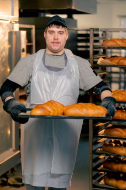 Profesyonel mutfakta kapsayıcı bir fırıncı hazır ekmeği tepside gülümseyerek bekliyor.