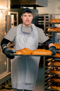 Profesyonel mutfakta kapsayıcı bir fırıncı hazır ekmeği tepside gülümseyerek bekliyor.
