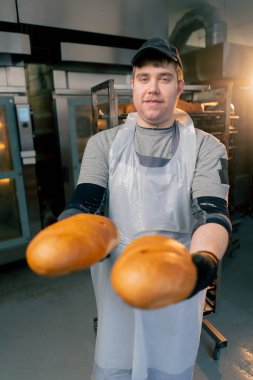 Profesyonel bir mutfakta fırıncıların elleri siyah eldivenlerle ekmeği tutar ve gülümserler.