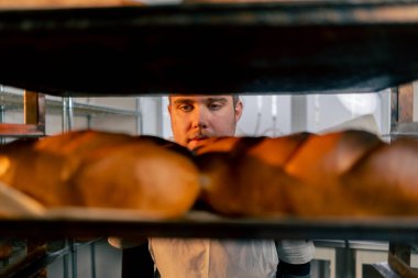 Profesyonel bir mutfakta, bir fırıncının elleri raftan bir tepsi ekmek alır.