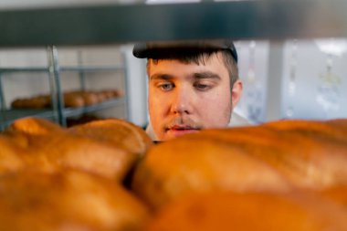 Profesyonel bir mutfakta yakın plan bir fırıncı raftan bir tepsi ekmeğe bakar.