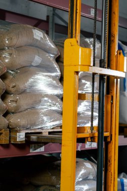 Kahve fabrikasında çalışan bir işçi, paleti almak için sarı bir forkliftle gelir.
